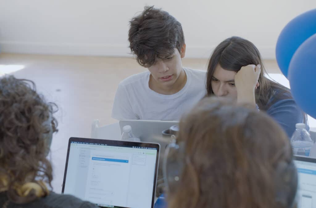 Students huddle over their laptops in collaborative group work.