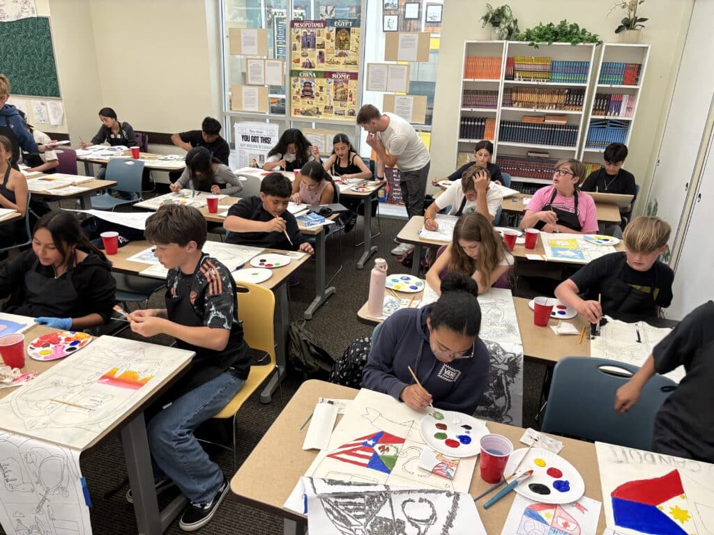 Middle school students in art class work on their projects at desks together.