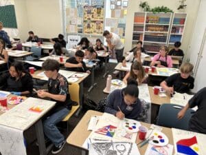 Middle school students in art class work on their projects at desks together.