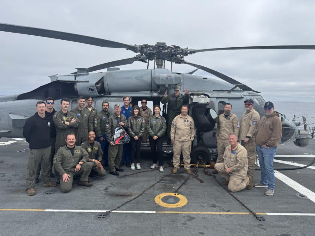 Navy crew members pose with helicopter in background.