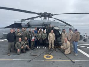Navy crew members pose with helicopter in background.